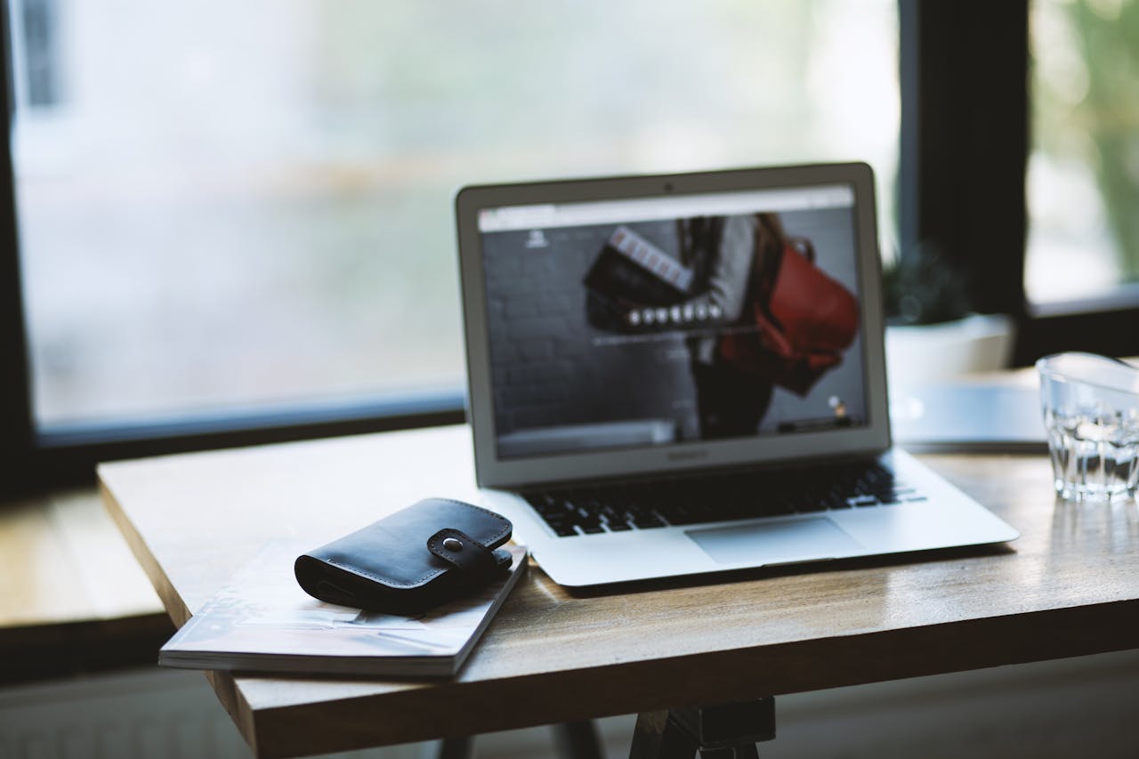 A contemporary workspace featuring a laptop and wallet on a wooden desk, near a window with natural light.