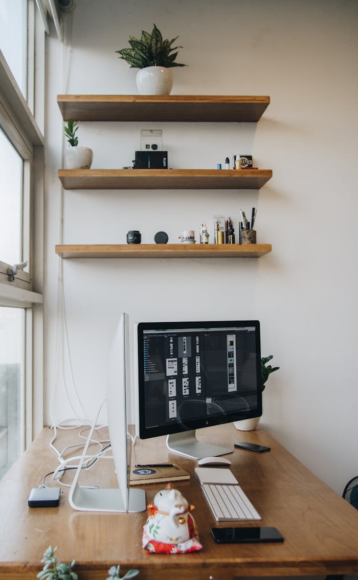 A sleek office workspace featuring a computer, shelves, and minimalist decor.